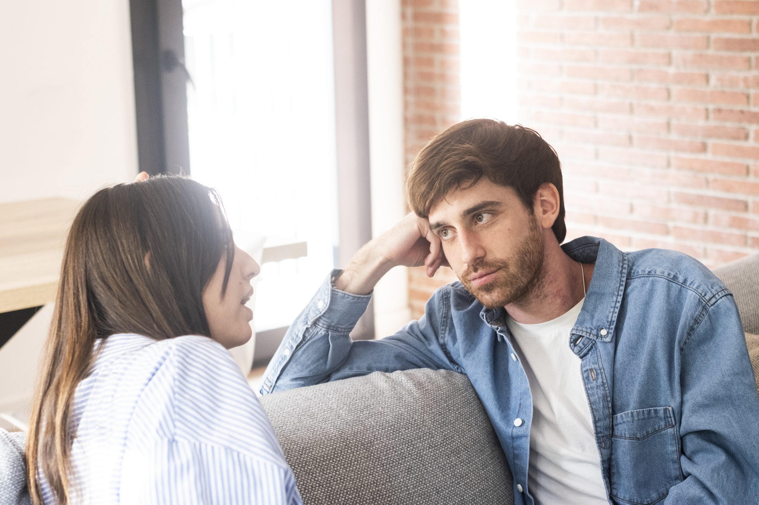 A young 25-year-old couple sits on their cozy sofa in a living room, engaged in a quiet conversation and sharing carefree moments together. Leisure and relaxation concept. Discussion man and woman